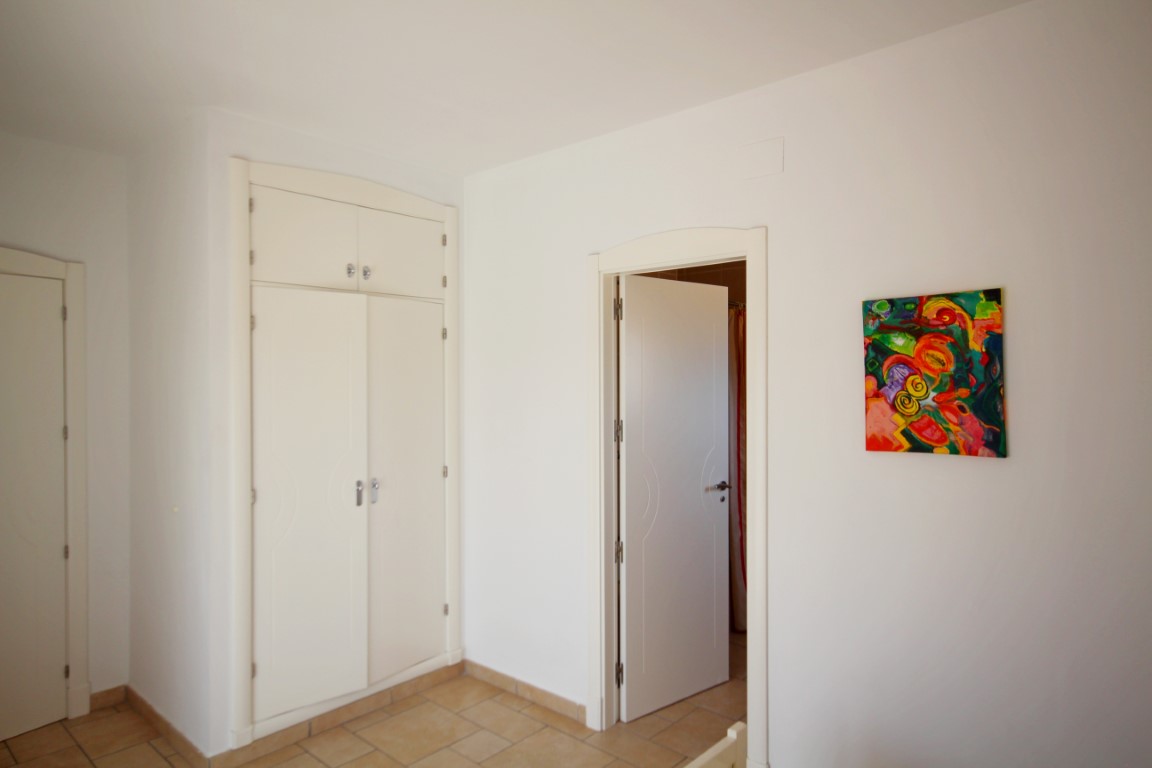 Dormitorio con armario empotrado blanco, suelos cerámicos en tonos tierra y paredes blancas decoradas con arte contemporáneo.