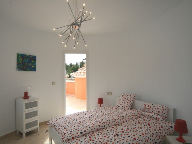 Dormitorio con paredes curvas, cama doble con textiles de colores, lámpara de diseño y salida directa a la terraza superior.