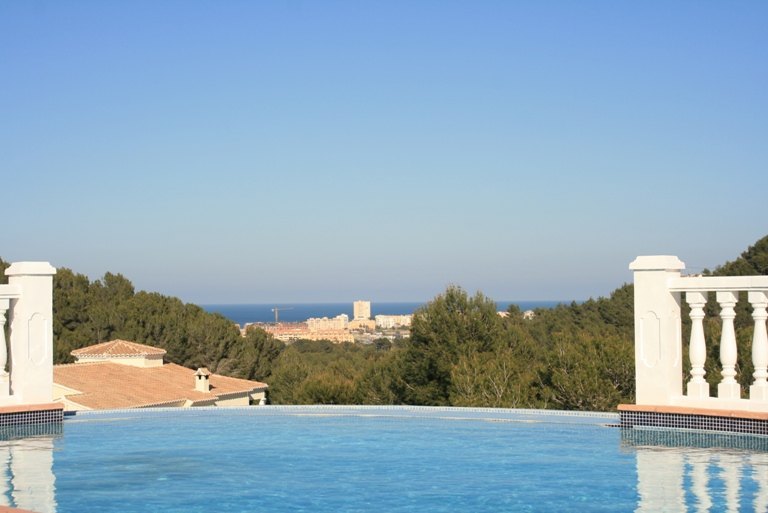 Piscina infinita con borde de gresite azul y balaustrada blanca, ofreciendo vistas panorámicas al mar Mediterráneo y al entorno forestal de Jávea.