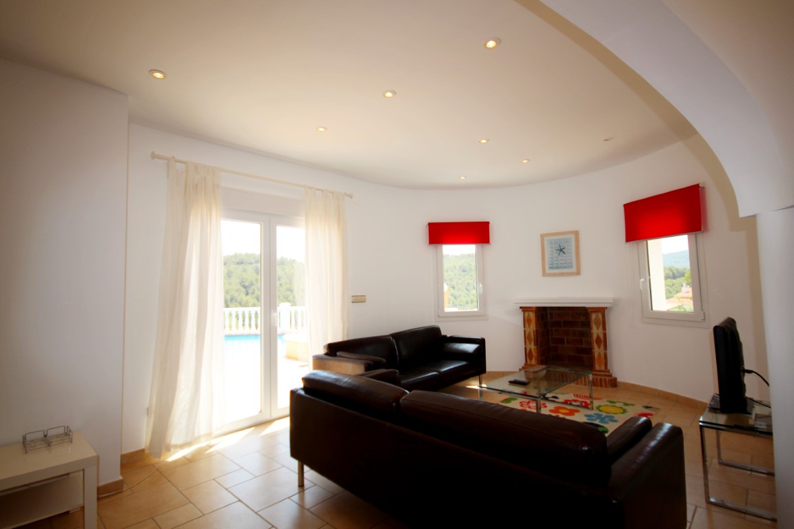Salón con sofás de cuero oscuro, chimenea de obra y acceso directo a la terraza. La estancia cuenta con iluminación empotrada y suelos cerámicos.