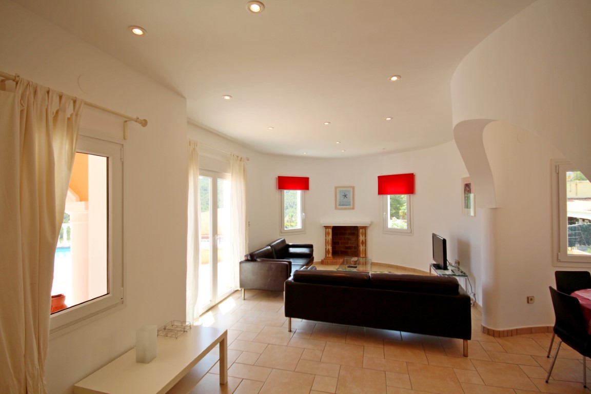 Salón luminoso con paredes curvas, chimenea de obra y suelos cerámicos. Dispone de acceso directo a la terraza y techos con iluminación empotrada.