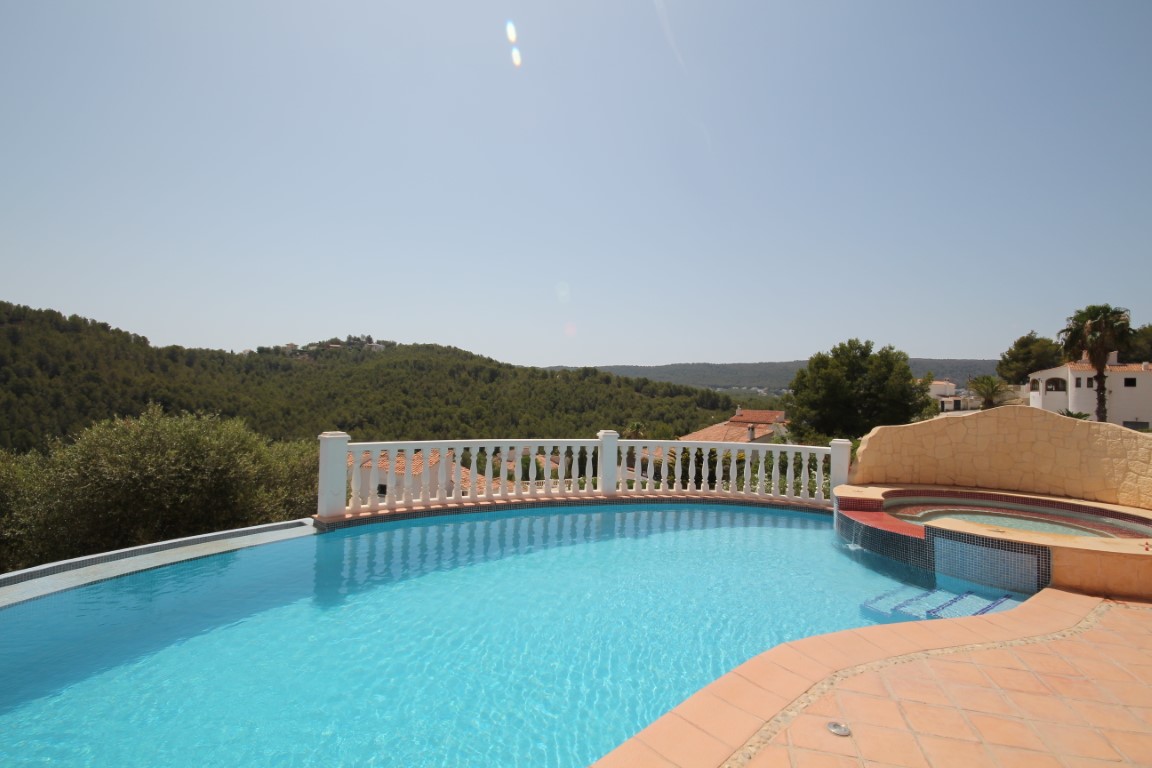 Terraza solárium con piscina infinita de borde curvo, jacuzzi integrado y vistas panorámicas a las colinas circundantes bajo un cielo despejado.