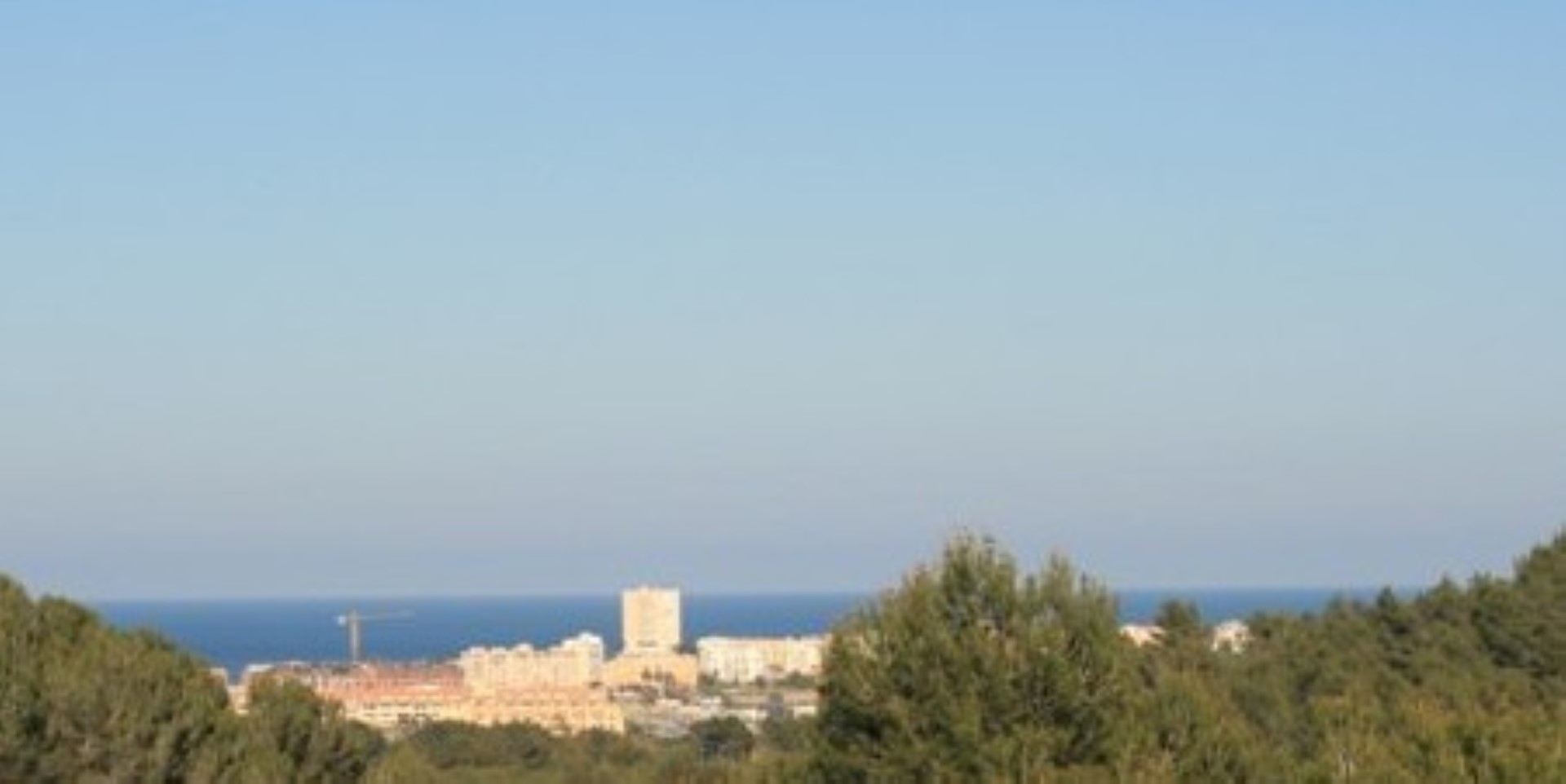 Vistas panorámicas al mar Mediterráneo y al entorno urbano costero desde una posición elevada, rodeada de pinos y vegetación autóctona.