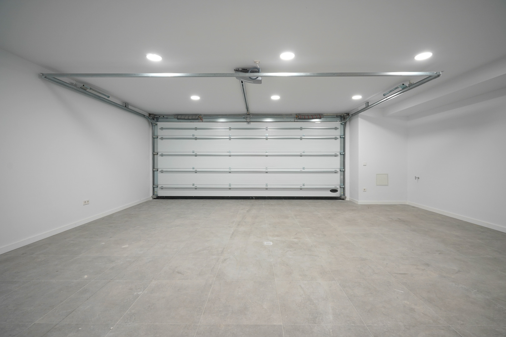Amplio garaje para dos coches con puerta automática seccional, suelo de gres gris e iluminación LED integrada en el techo.