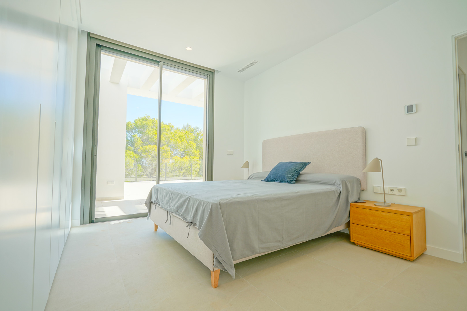 Dormitorio luminoso con ventanales de suelo a techo, acceso directo a la terraza con pérgola, armarios empotrados blancos y vistas al entorno boscoso.