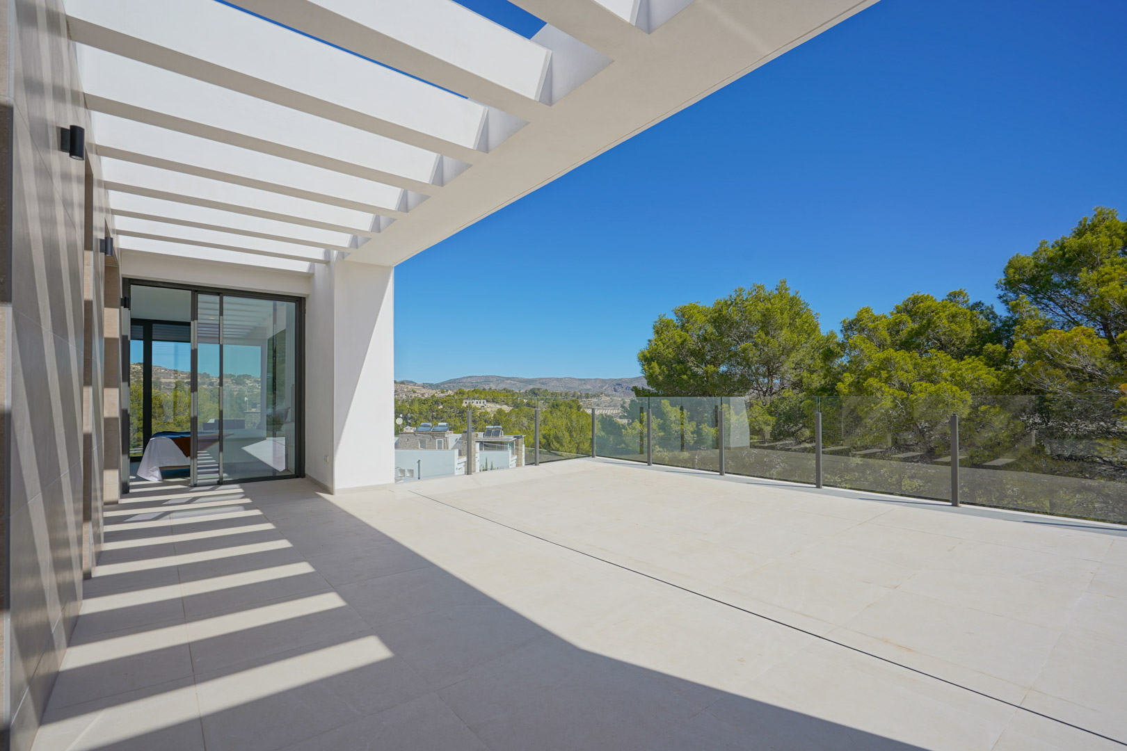 Terraza superior con pérgola blanca y barandilla de cristal, ofreciendo vistas abiertas a la zona boscosa y acceso directo al dormitorio mediante ventanales.