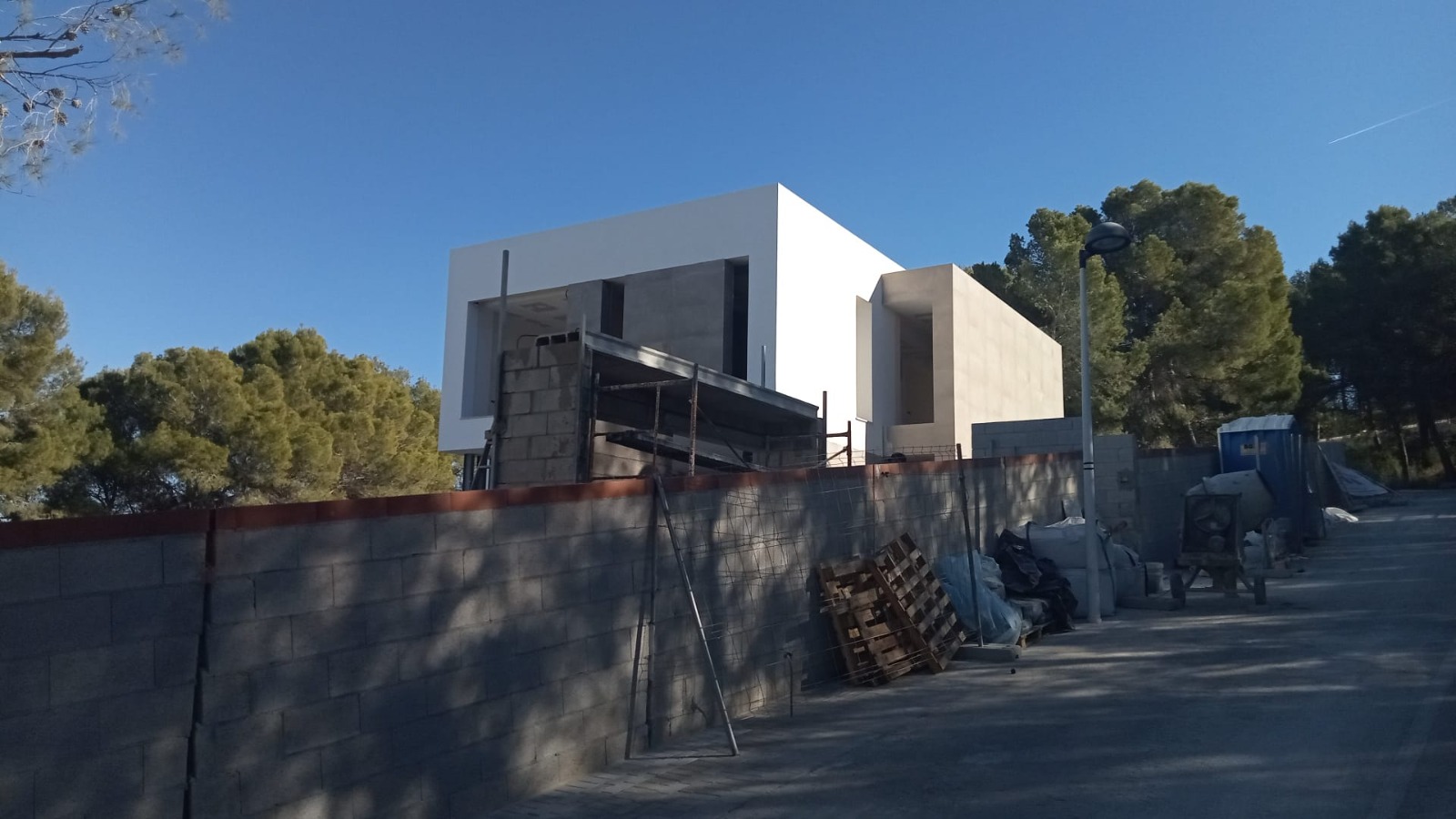 Vista exterior de la villa moderna en fase de construcción, destacando su arquitectura cúbica con acabados en piedra natural y su entorno boscoso.