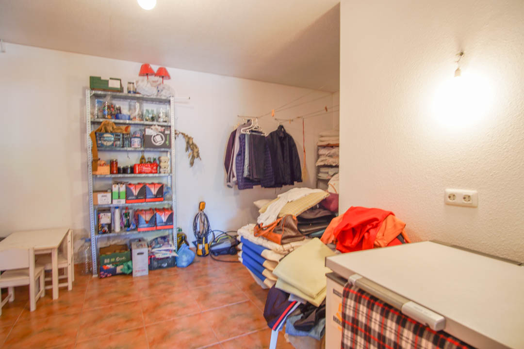 Amplio trastero en la planta baja con suelos cerámicos, estanterías metálicas y espacio funcional para almacenamiento y lavandería.