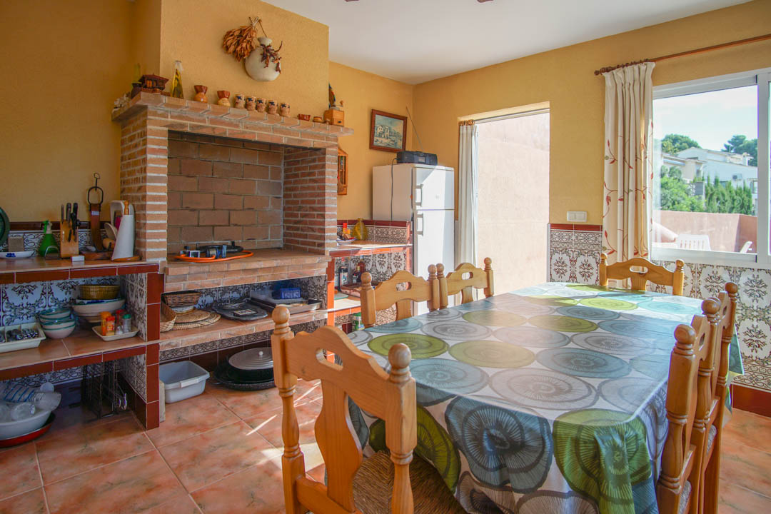 Cocina exterior cerrada con horno de leña de ladrillo visto, encimeras de azulejos tradicionales y zona de comedor con mesa de madera maciza.