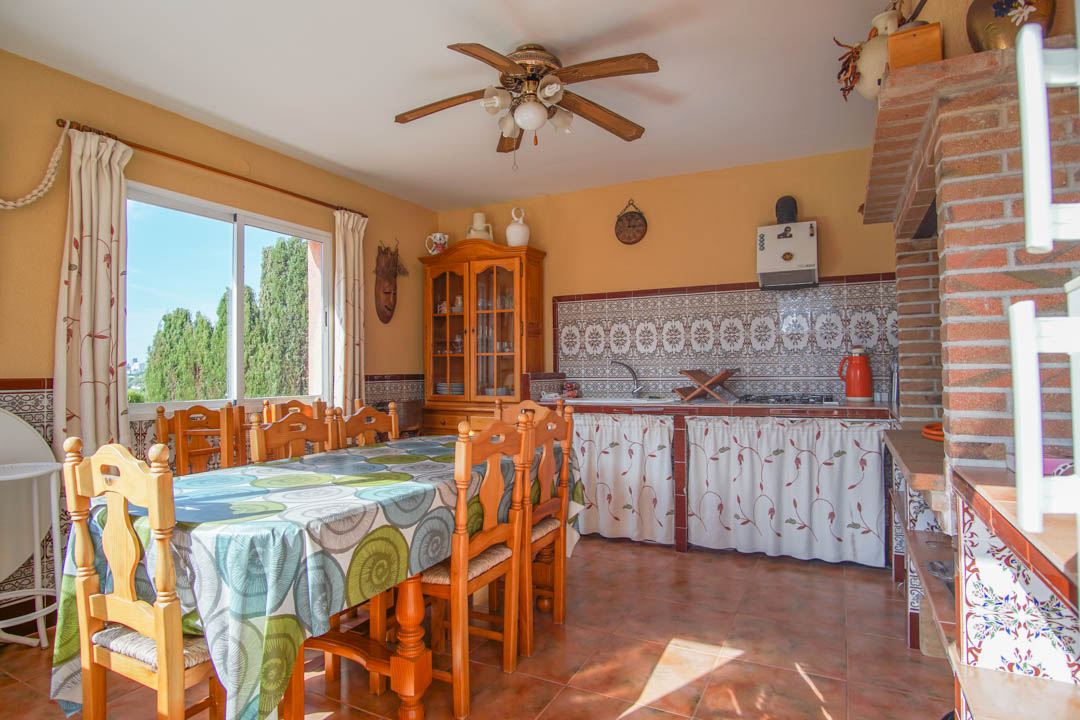 Cocina exterior cerrada con zona de comedor, destacando azulejos tradicionales, muebles de madera maciza y una estructura de ladrillo visto.