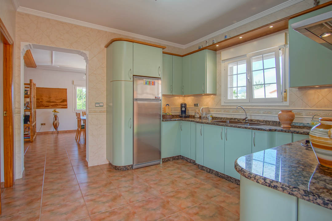 Cocina independiente con armarios en tono verde menta, encimeras de granito y electrodomésticos integrados. El suelo de gres conecta con el comedor a través de un arco.