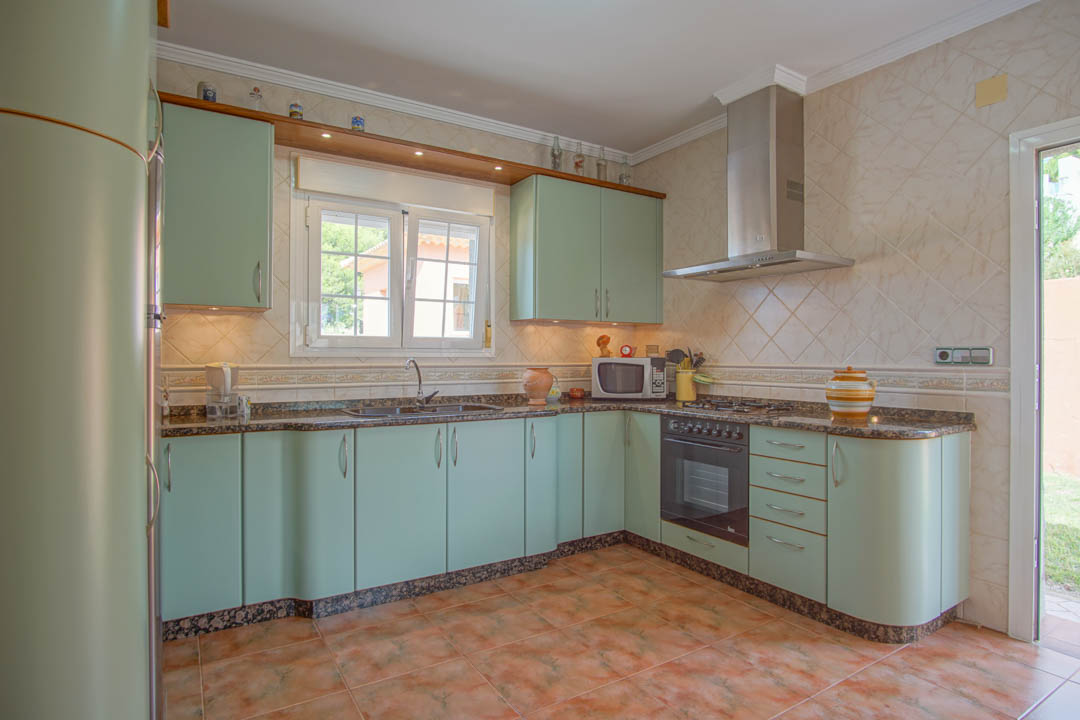 Cocina independiente con muebles en verde pálido, encimeras de granito y electrodomésticos integrados. Incluye campana de acero inoxidable y acceso directo al exterior.