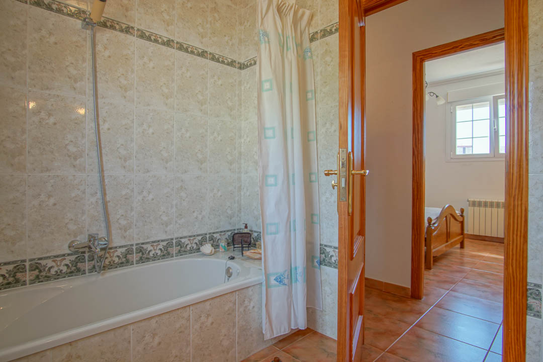 Cuarto de baño con bañera integrada, azulejos clásicos con cenefa decorativa y marcos de puertas en madera maciza que conectan con el dormitorio.