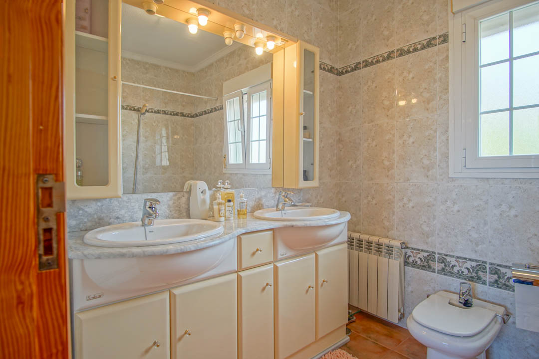 Cuarto de baño con lavabo de doble seno sobre encimera de mármol, armarios integrados con espejos iluminados y paredes alicatadas con cenefa decorativa.