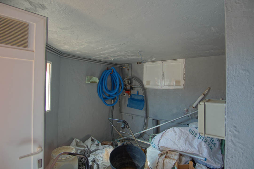 Cuarto de mantenimiento y trastero con paredes en tono gris, equipado con manguera de piscina, herramientas de limpieza y acceso técnico organizado.