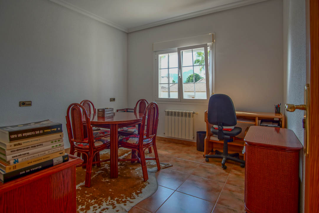 Despacho luminoso con suelos de gres, mesa de madera maciza y zona de escritorio. La ventana ofrece luz natural y vistas despejadas al entorno residencial.