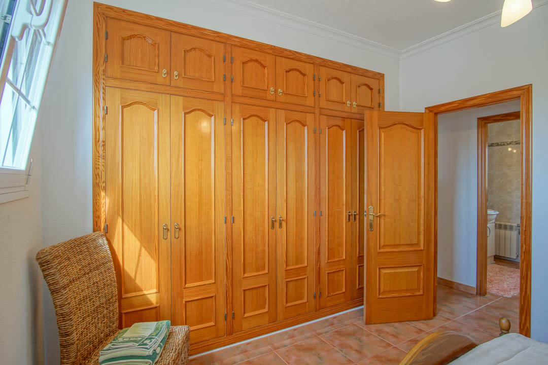 Dormitorio con amplio armario empotrado de madera maciza de suelo a techo y puertas interiores a juego sobre suelo cerámico.