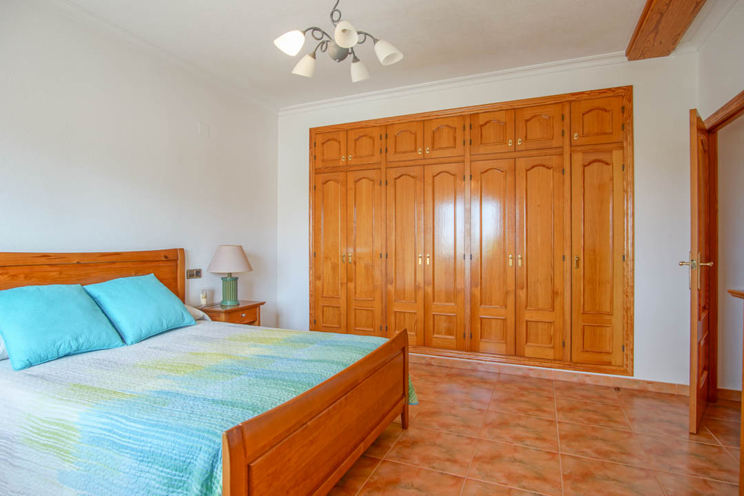 Dormitorio con amplios armarios empotrados de madera maciza a medida, suelos de gres rústico y carpintería interior coordinada de alta calidad.