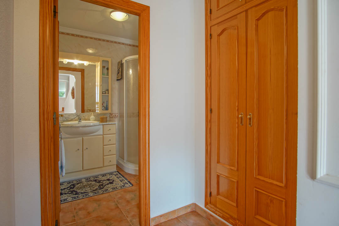 Dormitorio con armario empotrado de madera maciza y acceso a un baño con ducha de esquina, encimera de mármol y azulejos decorativos.