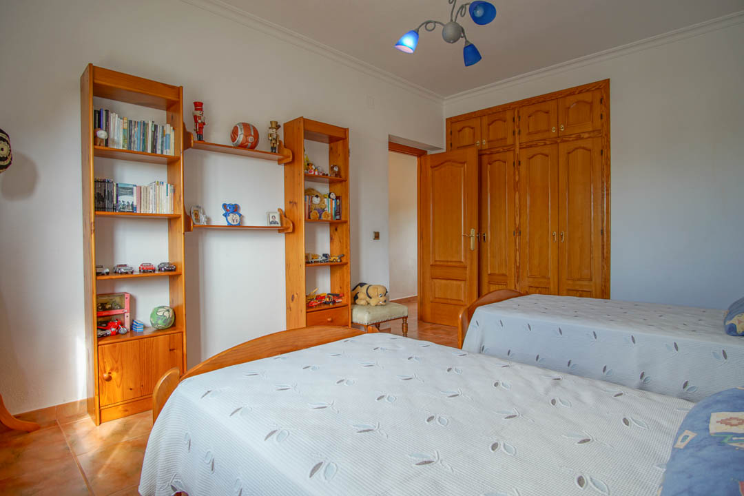 Dormitorio con dos camas individuales, estanterías de madera maciza y armarios empotrados a medida con acabados artesanales y suelos de gres.