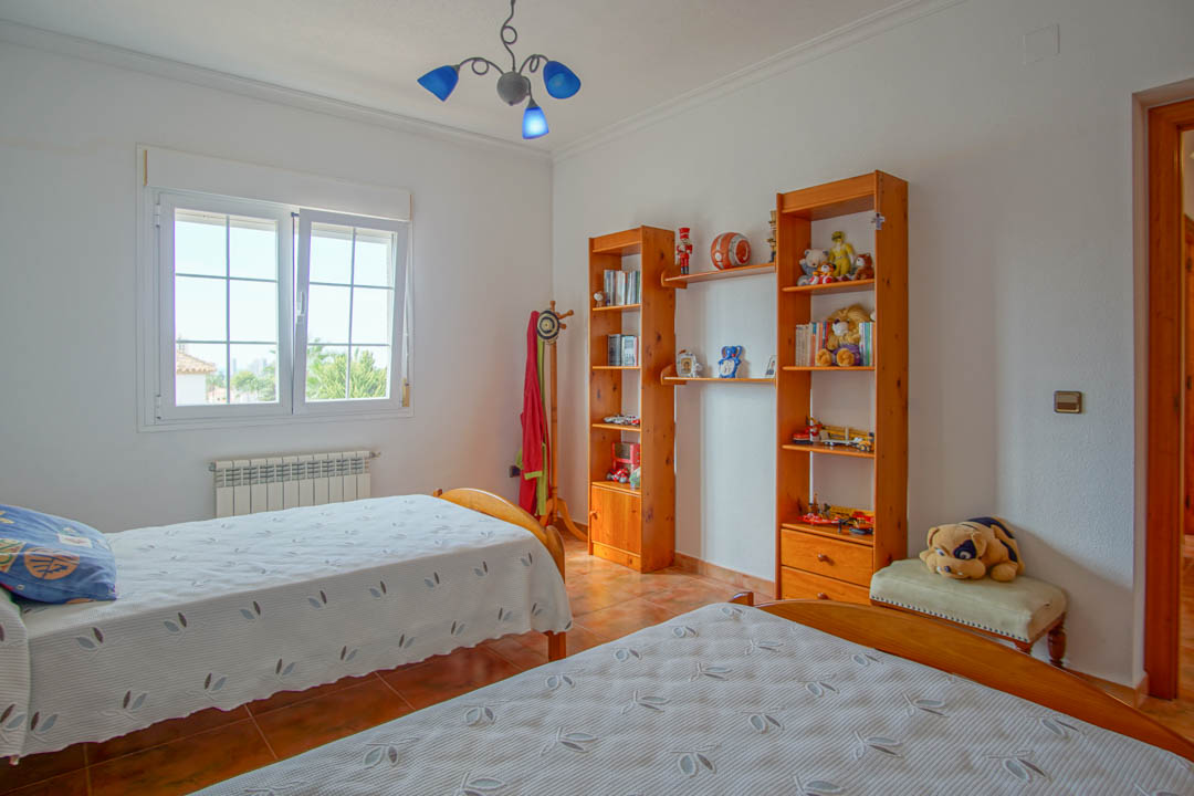Dormitorio con dos camas individuales, estanterías de madera maciza y suelos cerámicos. Dispone de radiador y ventana de PVC con doble acristalamiento para luz natural.