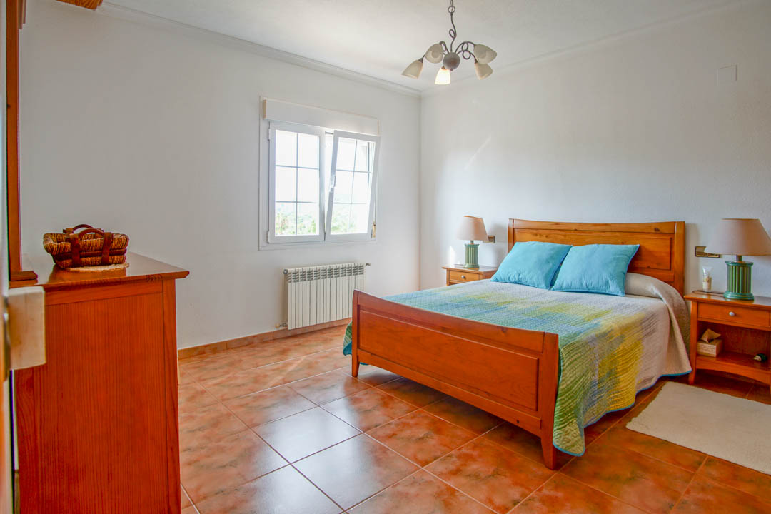 Dormitorio con mobiliario de madera maciza, suelos de gres rústico y ventana de doble acristalamiento con radiador inferior para mayor confort.