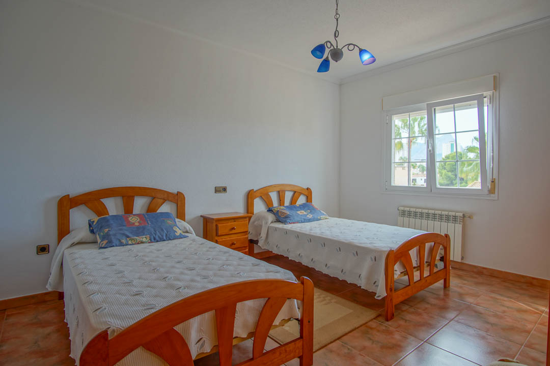 Dormitorio luminoso con dos camas de madera maciza, suelos de gres y ventana de doble acristalamiento con vistas a la montaña y palmeras.