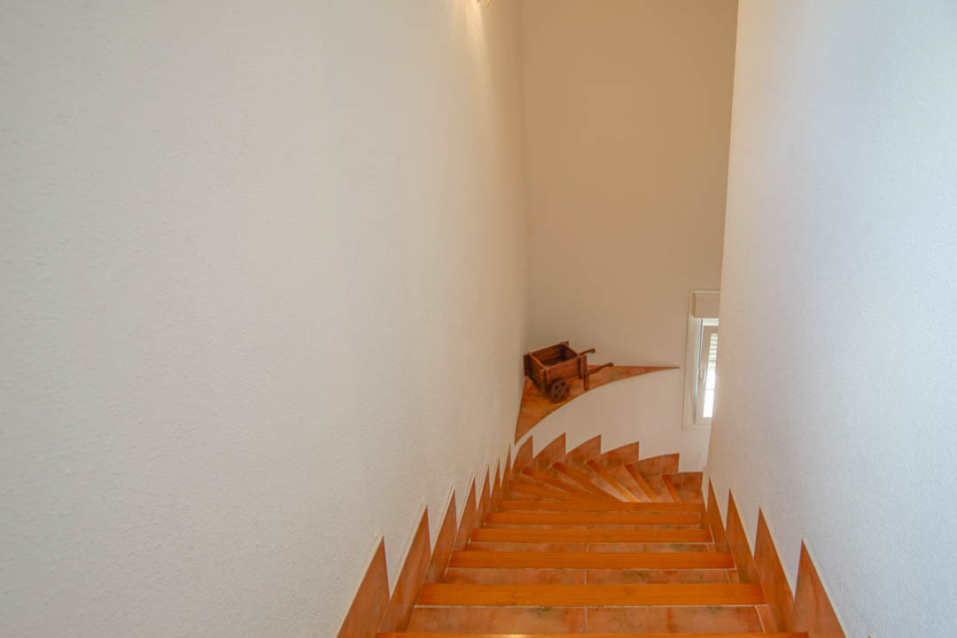 Escalera interior con peldaños de gres cerámico y bordes de madera, conectando las plantas entre paredes blancas de acabado rugoso.