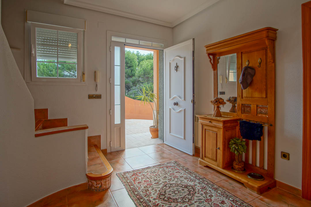 Hall de entrada con suelos de gres cerámico, mueble recibidor de madera maciza y acceso directo desde el exterior a través de una puerta blanca decorada.