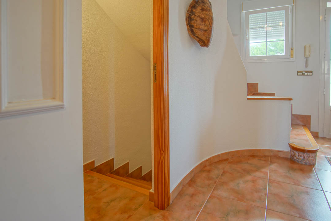 Hall de entrada con suelos de gres y carpintería de madera maciza, conectando los niveles de la vivienda a través de una escalera interior.
