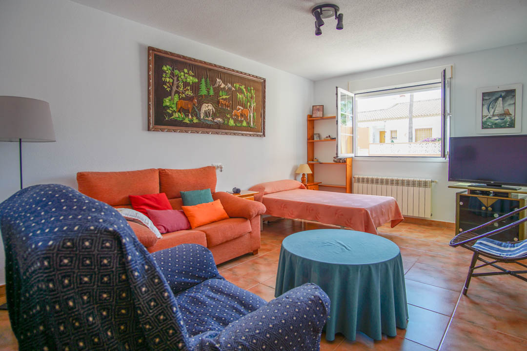 Sala de estar con suelos cerámicos, sofá en tonos cálidos y cama individual. Incluye ventanal de doble hoja que aporta luz natural y calefacción por radiador.