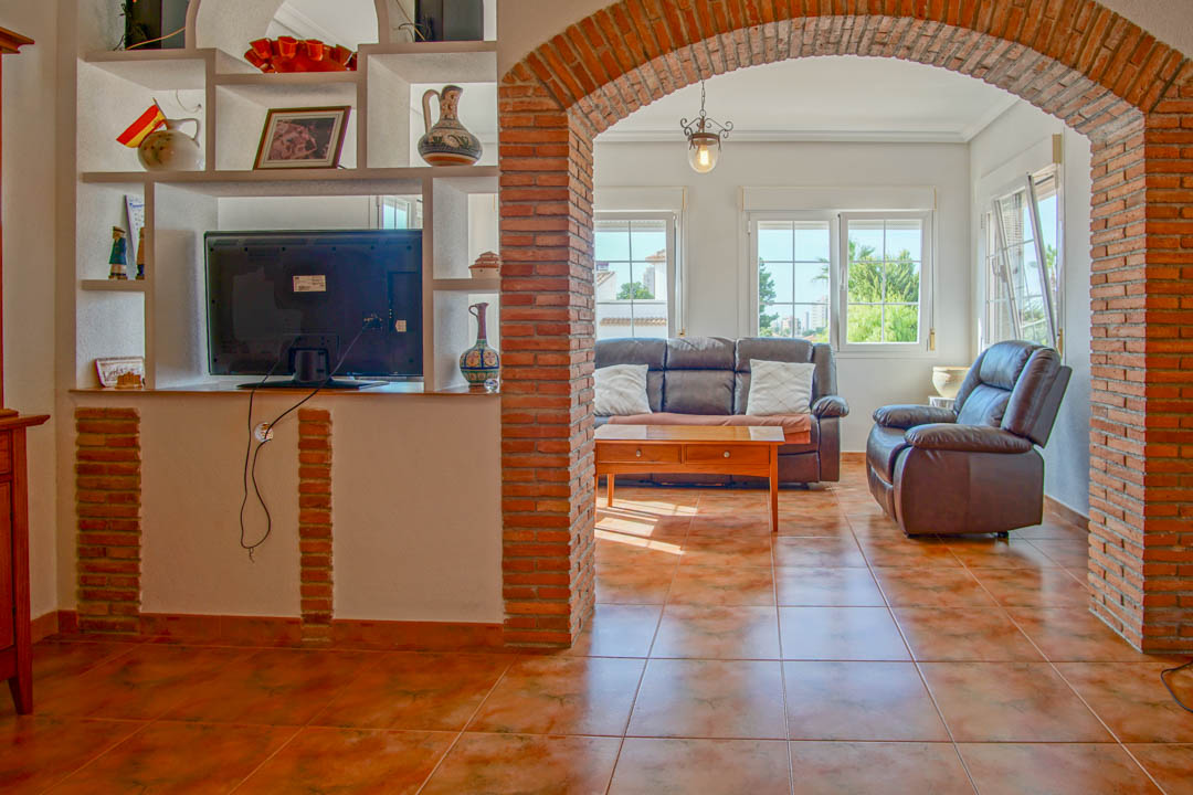 Salón con suelos de gres y un arco de ladrillo visto que conecta con una zona de estar luminosa equipada con sofás de cuero y estantería de obra.