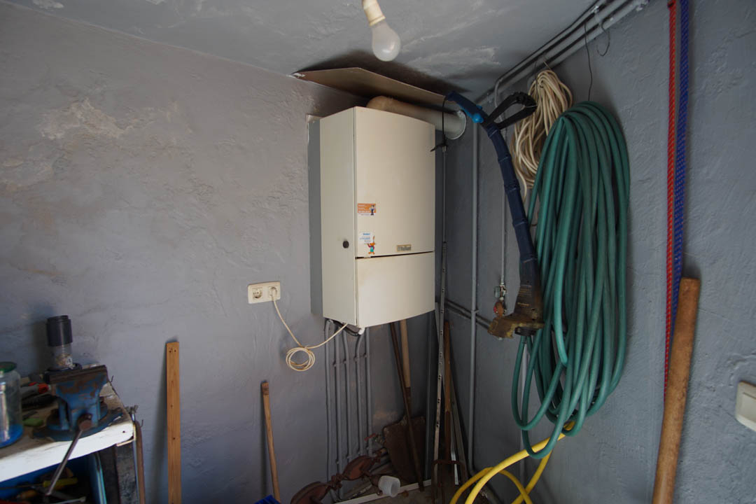 Trastero y cuarto técnico con caldera de pared Vaillant, zona de trabajo con banco y almacenamiento para herramientas de jardín.