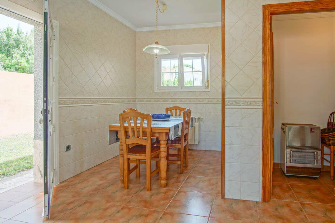 Zona de comedor con mesa y sillas de madera maciza, paredes alicatadas con azulejos decorativos y acceso directo al jardín exterior.
