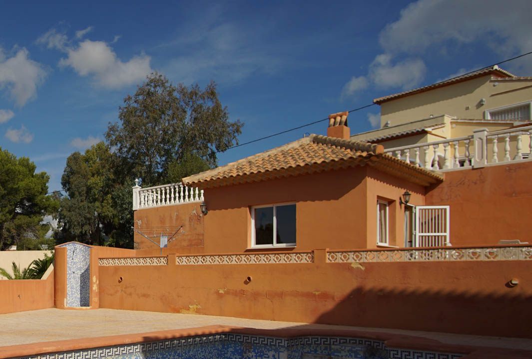 Zona de piscina con ducha exterior de mosaico azul y un anexo independiente con tejado de teja tradicional y paredes en tono terracota.