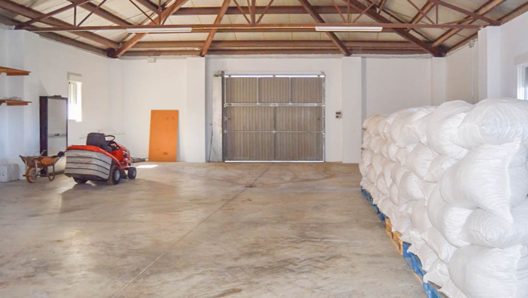 Amplio almacén agrícola con estructura de techo metálica, suelo de hormigón, maquinaria de mantenimiento y zona de almacenaje para la cosecha ecológica.