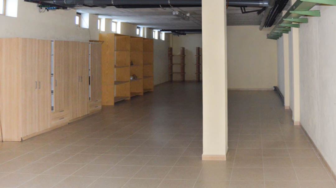 Amplio espacio de almacenamiento en el garaje subterráneo con suelos cerámicos, armarios de madera y estanterías abiertas bajo instalaciones técnicas vistas.