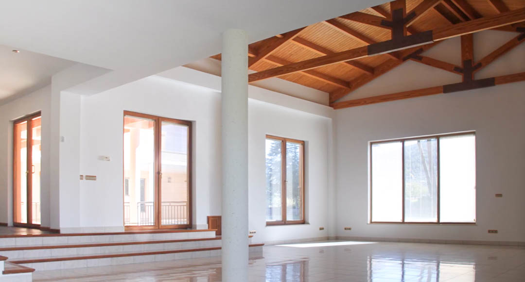 Amplio salón diáfano con techos altos de madera vista, suelos de gres pulido y grandes ventanales que inundan el espacio de luz natural.