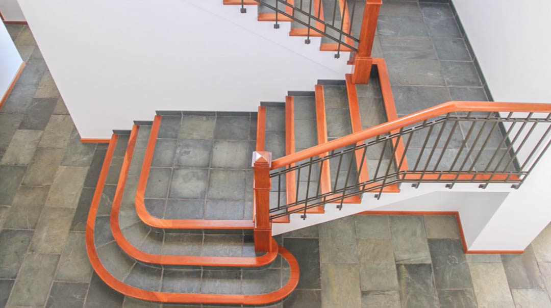 Escalera interior con peldaños de piedra natural y bordes de madera noble. Destaca su barandilla metálica con pasamanos de madera y el suelo de pizarra coordinado.