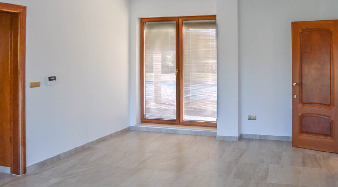 Habitación con suelos de gres, carpintería de madera de alta calidad en puertas y ventanas, y vistas al exterior a través de persianas integradas.