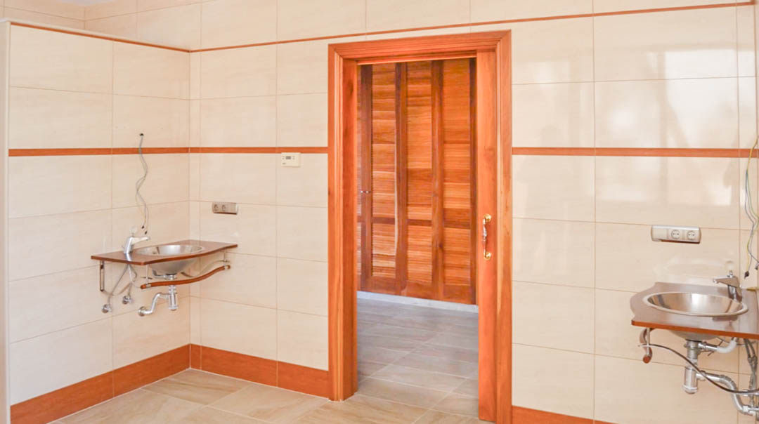 Sala de preparación con paredes alicatadas, dos lavabos de acero inoxidable sobre soportes de madera y acceso a una estancia con carpintería de alta calidad.