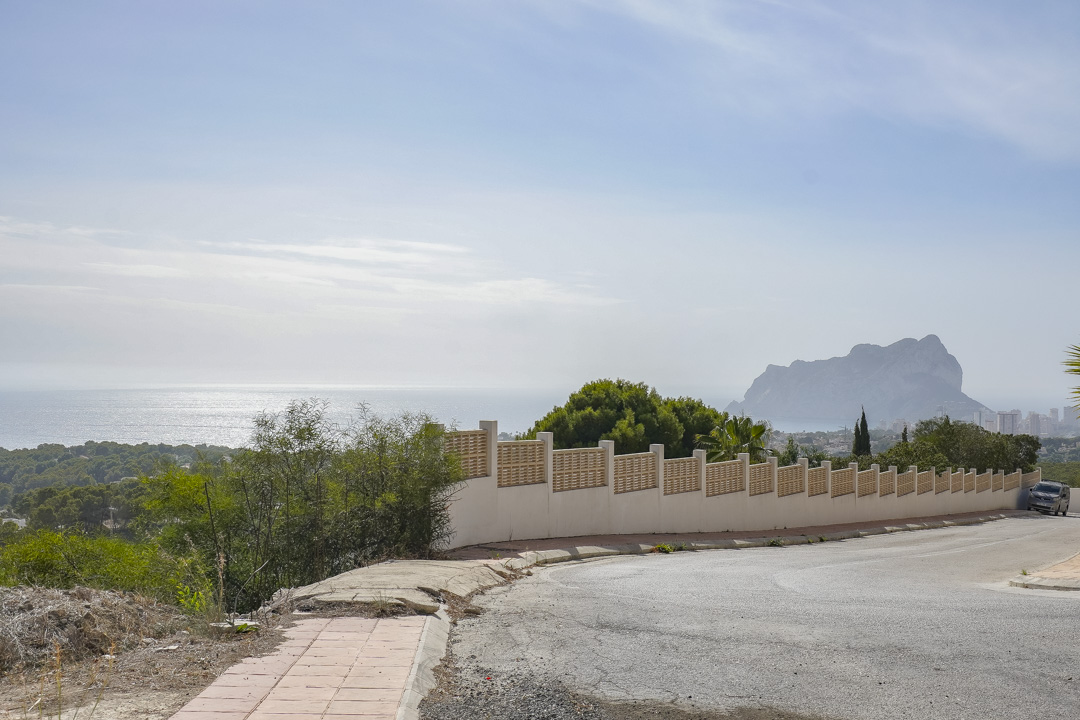 Vista desde el acceso a la propiedad que muestra el Peñón de Ifach sobre el horizonte marino, junto a un muro perimetral blanco con vallado de celosía.