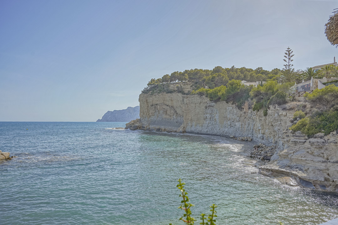 Vista panorámica de los acantilados de piedra caliza y aguas turquesas de la costa de Benissa, con vegetación mediterránea autóctona sobre el litoral.