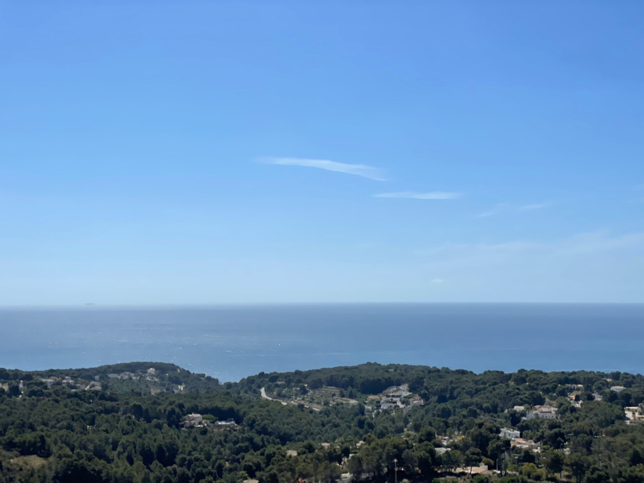 Vista panorámica elevada hacia el mar Mediterráneo sobre el paisaje arbolado de Benissa, destacando el horizonte despejado y la vegetación local.