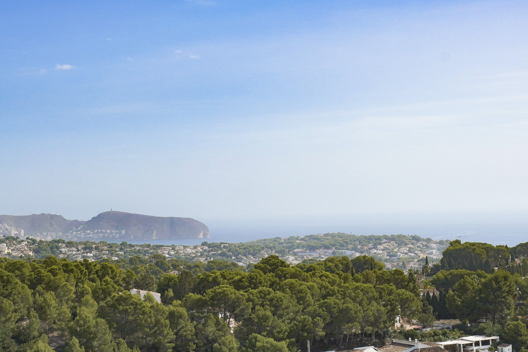 Vistas panorámicas de la costa de Benissa, destacando el cabo Cap D'or en Moraira sobre un extenso bosque de pinos mediterráneos y el mar azul.