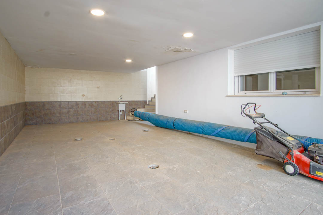 Amplio garaje con suelos cerámicos, iluminación empotrada y acceso directo a la vivienda. Incluye zona de lavadero con fregadero y espacio para maquinaria de jardín.