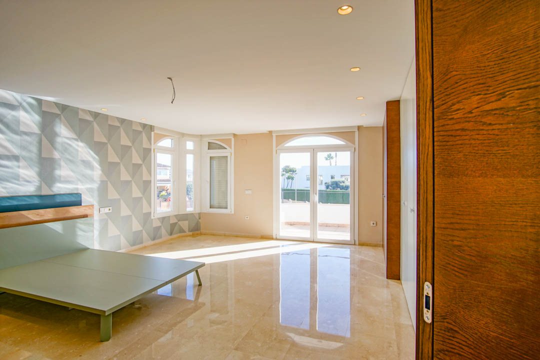 Dormitorio amplio con suelos de mármol pulido, pared decorativa con patrón geométrico y acceso directo a una terraza soleada a través de puertas acristaladas.