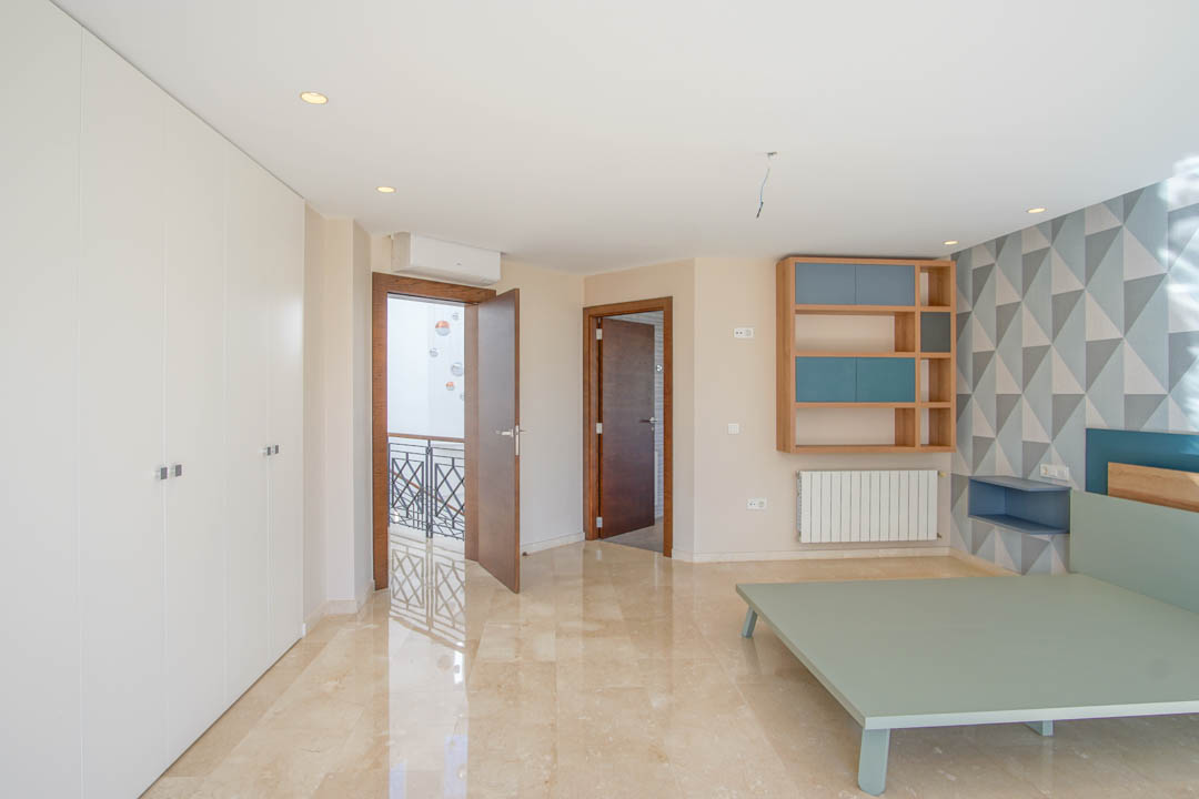 Dormitorio con suelos de mármol pulido, amplios armarios empotrados blancos y una pared de acento geométrica. Incluye estantería de madera integrada y acceso al rellano.