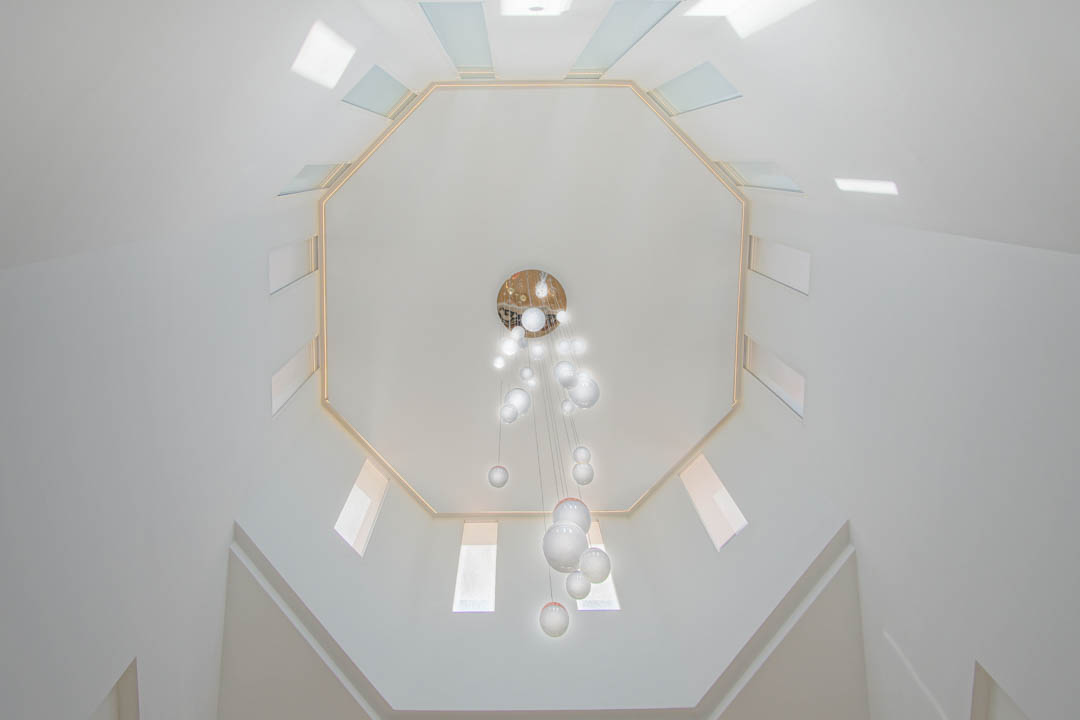 Vista cenital de la cúpula octogonal con tragaluces simétricos y una lámpara colgante de esferas de cristal en el hueco de la escalera de doble altura.