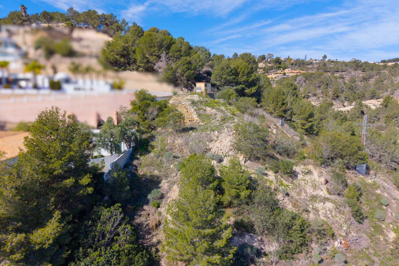 Parcela escarpada en Tossal Los Bancales con vegetación mediterránea, pinos y acceso a suministros, situada en una ladera con vistas despejadas.